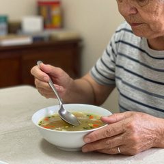 A woman in her eighties eating a bowl of vegetable soup at a table