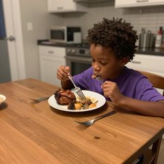 A child about six years old eating a plate of roast dinner at a table